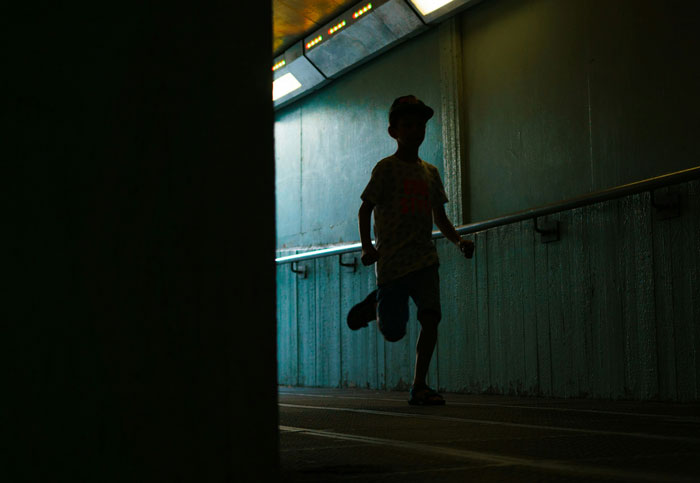 Silhouetted child running through dimly lit tunnel captured by security camera in an urban setting.