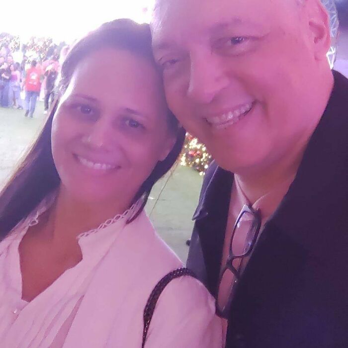 Couple smiling at an outdoor event with festive lights in the background under soft purple lighting. Couple smiling at an outdoor event with festive lights in the background under soft purple lighting.