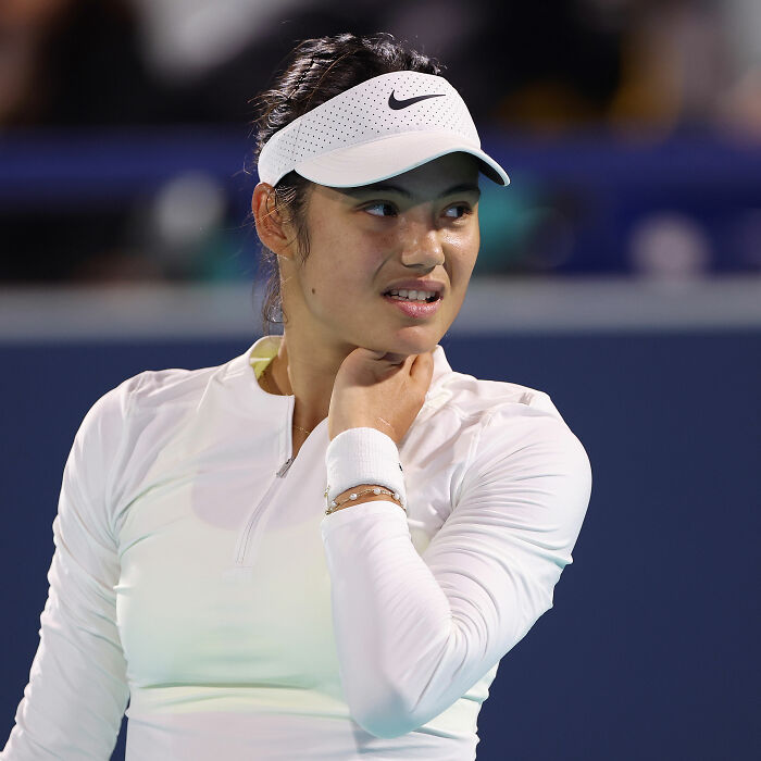 Tennis star wearing a white visor and sportswear, pausing on court with a concerned expression during match.