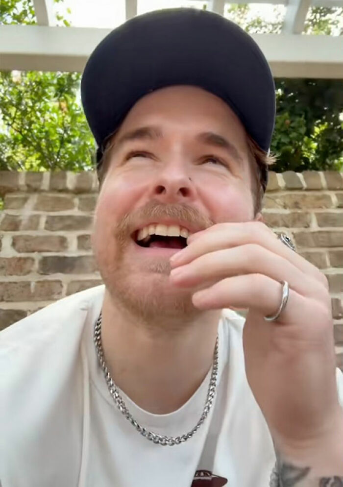 Young man wearing a cap and necklace laughing outdoors, highlighting short king and height preferences in dating discussions.