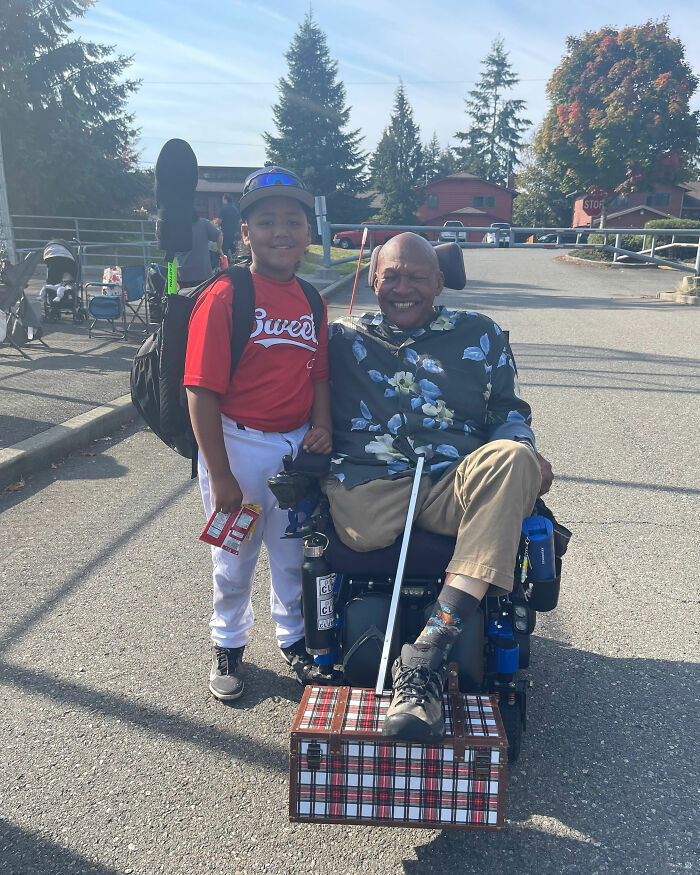 Black disabled veteran in a wheelchair smiling outdoors with a young boy in a baseball uniform on a sunny day. Black disabled veteran in a wheelchair smiling outdoors with a young boy in a baseball uniform on a sunny day.