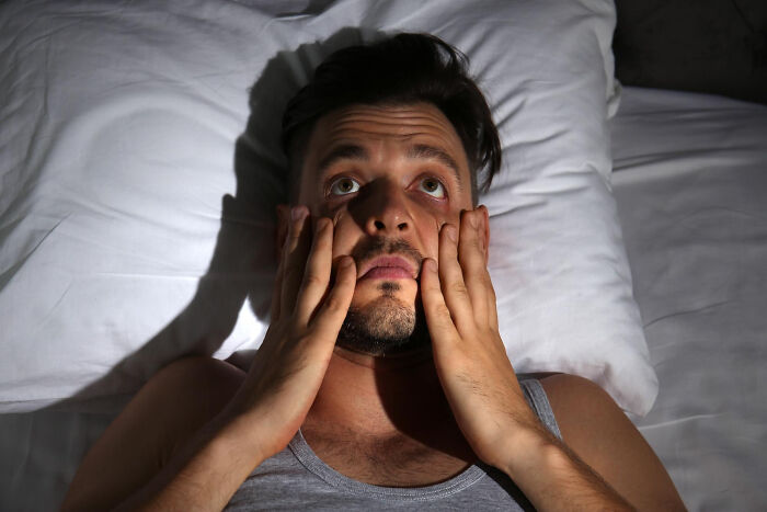 Man lying awake in bed at night looking scared and stressed after hearing the scariest sounds ever heard by people.
