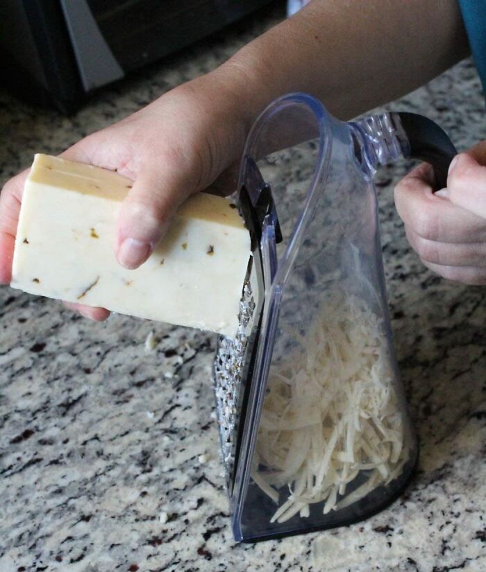 Person using a smart kitchen tool to grate cheese into a container on a granite countertop.