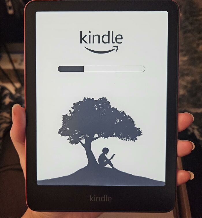 Kindle e-reader held in hand with loading screen showing a child reading under a tree for back to school finds.