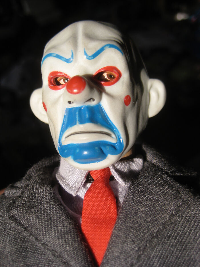 Creepy clown mask with sad expression worn by figure in grey suit and red tie, evoking disturbing home police stories.