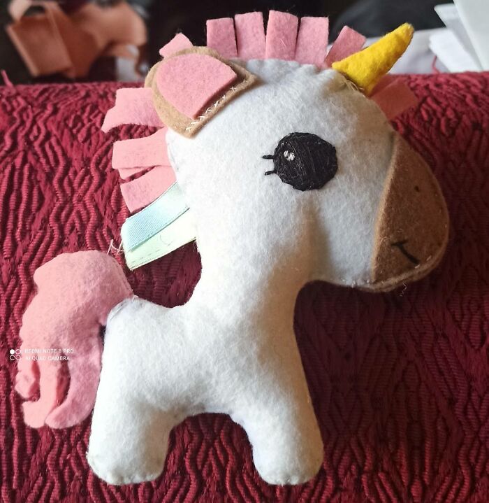 Handmade DIY unicorn plush with uneven stitching and mismatched details, showcasing a craft shaming example on a red textured surface.