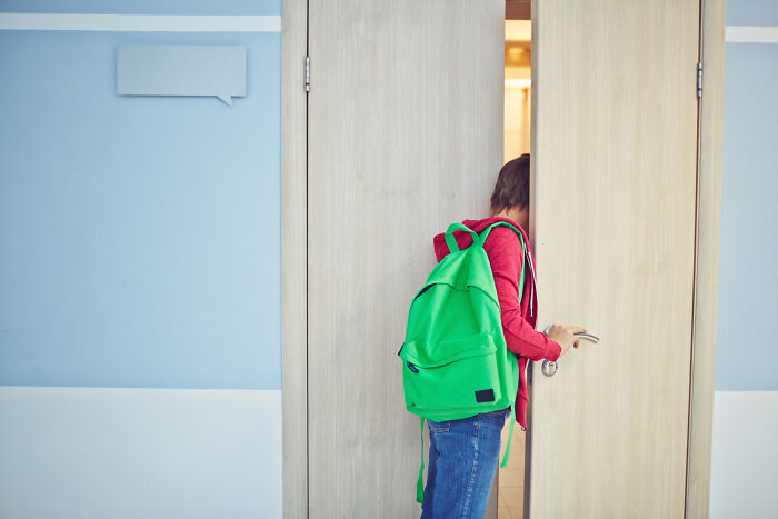 School kid with a green backpack confidently opening a door in a modern school hallway representing wildest things pulled off.