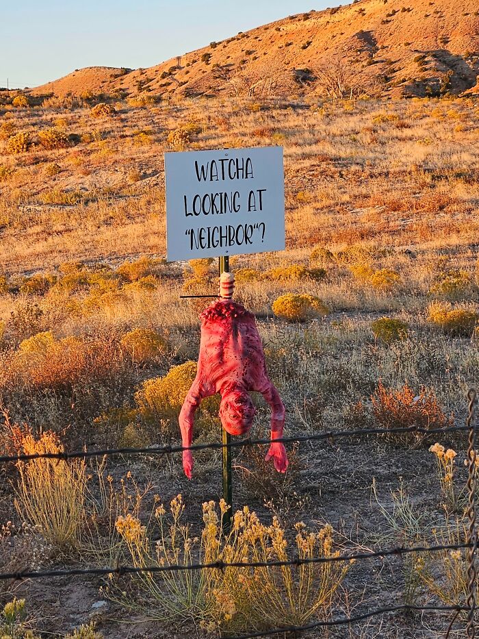 Creepy unhinged neighbor’s note with a disturbing figure and sign saying watcha looking at neighbor in a dry field.