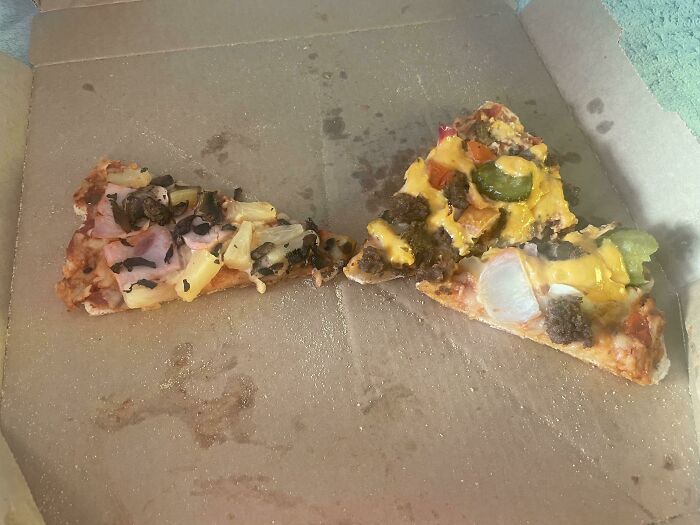 Two leftover pizza slices with unusual toppings inside a greasy pizza box seen in someone else’s home. - 20