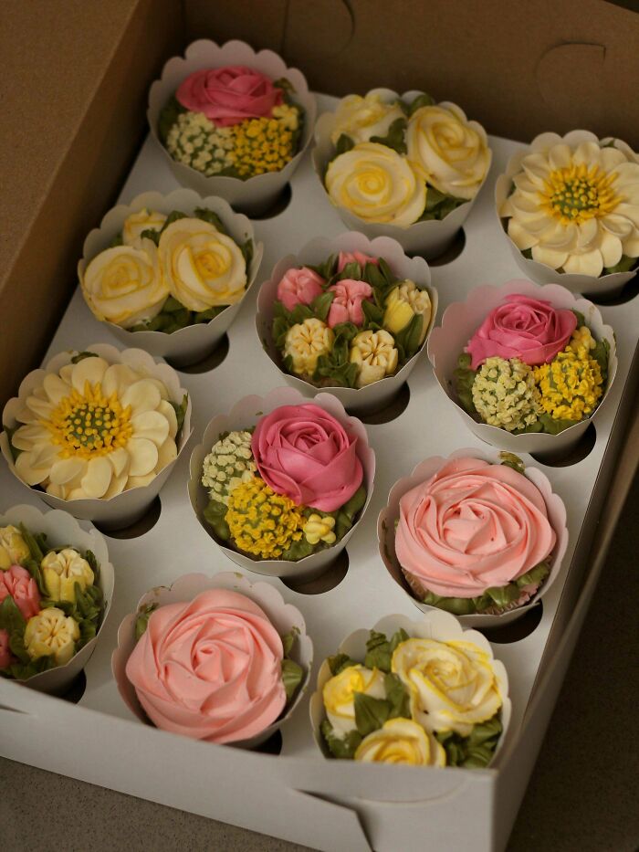 Box of gorgeous baked goods with intricate floral frosting designs in pink, yellow, and white colors.