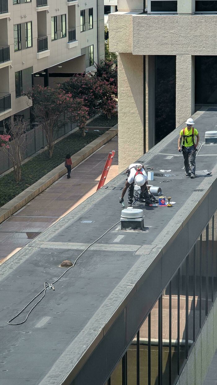 Two construction workers blatantly ignoring safety protocol while working on a high rooftop without proper fall protection.