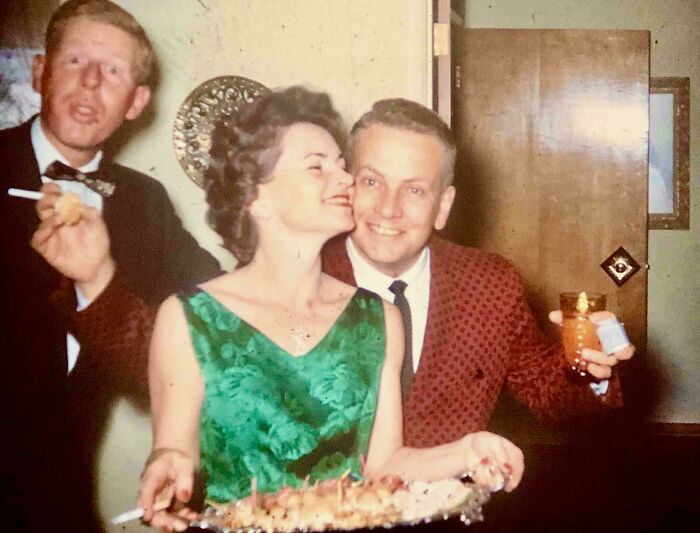 Candid glimpse into the past showing three people enjoying a party with drinks and appetizers in vintage attire.