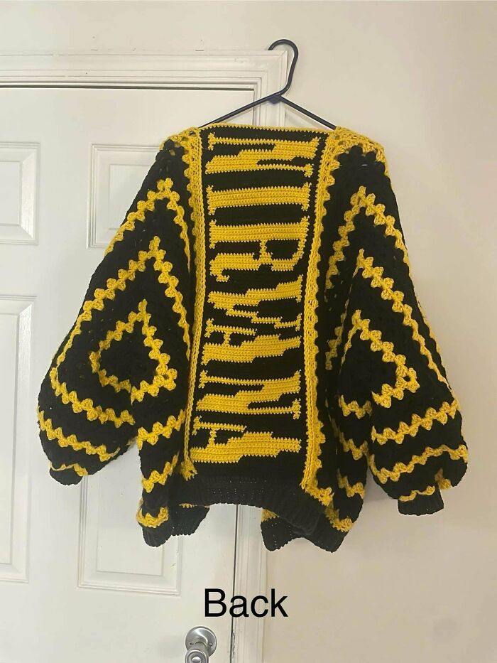 Black and yellow crochet sweater with bold geometric patterns hanging on a hanger, showcasing intricate crochet craftsmanship.