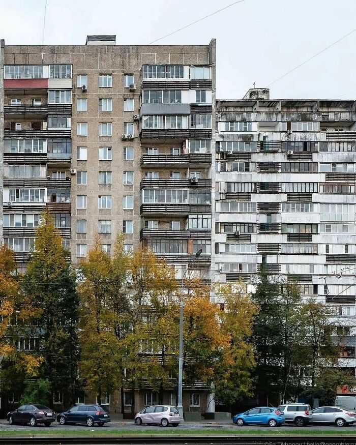 Worn and dilapidated apartment buildings with autumn trees and parked cars in an urban hell environment.