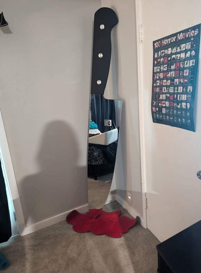 Knife-shaped mirror leaning against wall with a red mat shaped like a blood splatter, a funny example of awful taste but great e*******n.