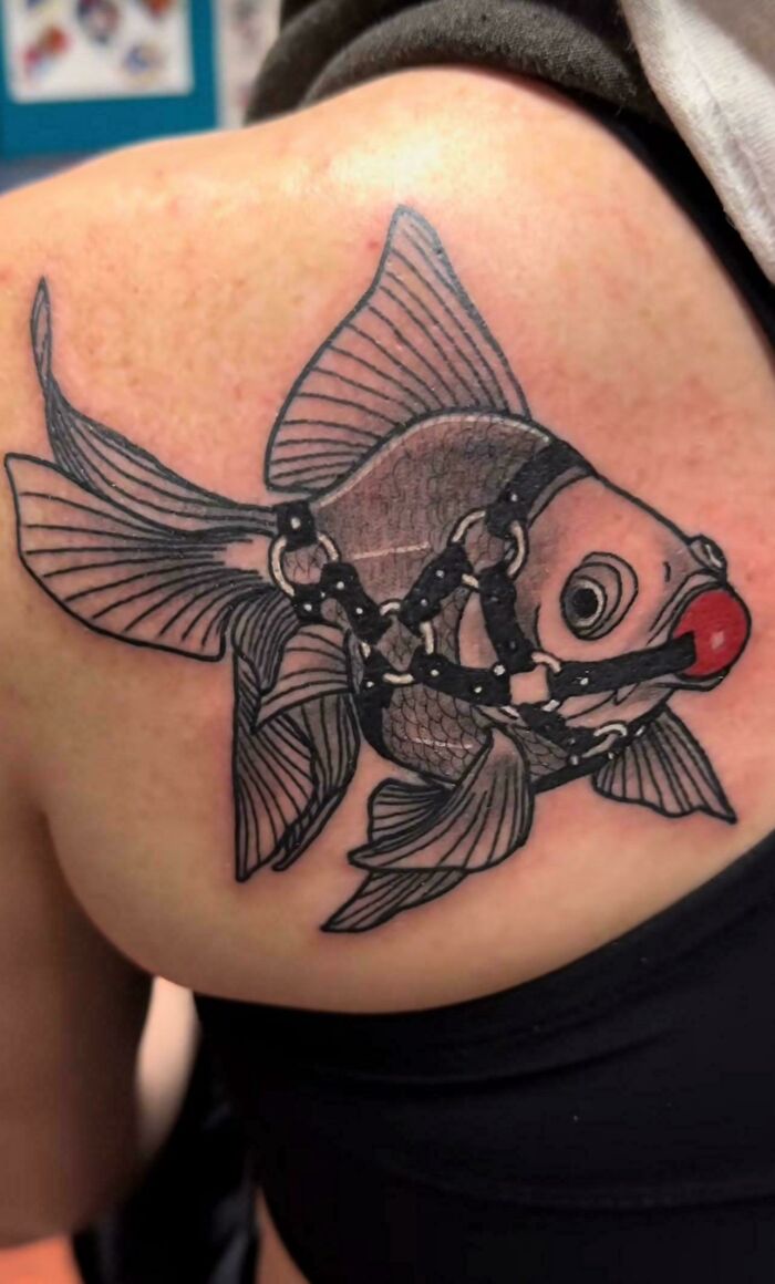 Tattoo of a detailed fish wearing a harness and gag, an example of awful taste but great e*******n tattoo art.