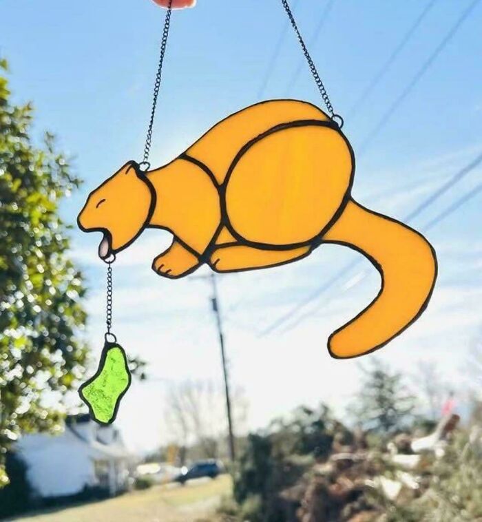 Awful taste but great e*******n stained glass cat hanging decoration with green fish charm outdoors in daylight.