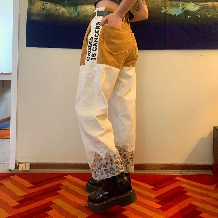 Person wearing white and brown pants with bold cancer warning text, standing on a red patterned carpet, showcasing awful taste but great e*******n.