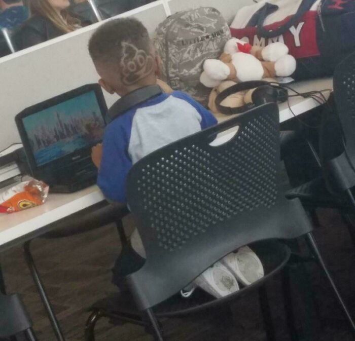 Young boy playing on a laptop with a funny awful taste haircut, showcasing great e*******n and unique style.