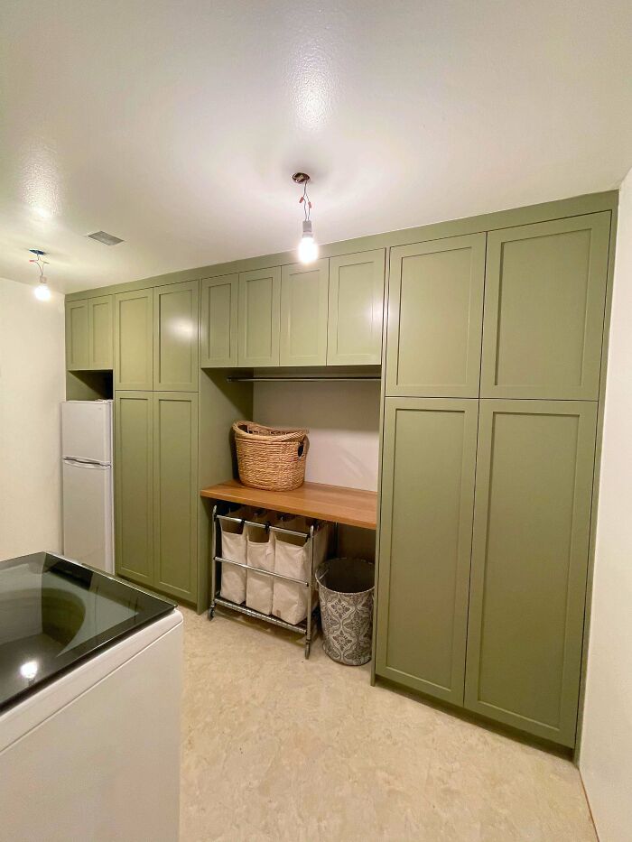 Organized laundry room with green cabinets, wooden countertop, and storage baskets showcasing proud home decoration.