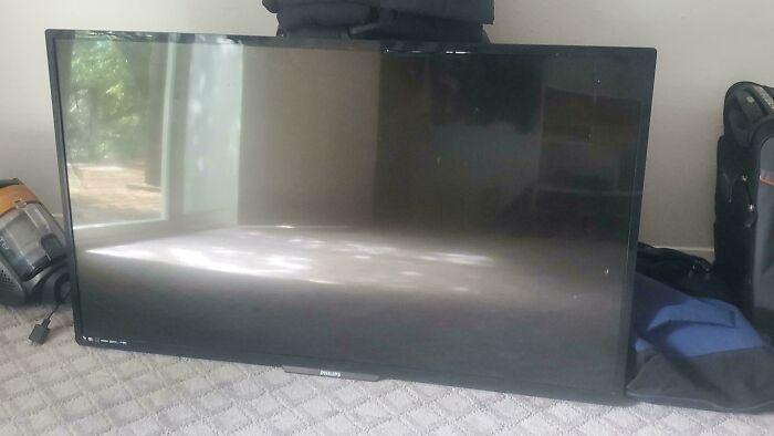 Flat screen Philips TV resting on carpeted floor among other household items, a potential dumpster diving treasure.