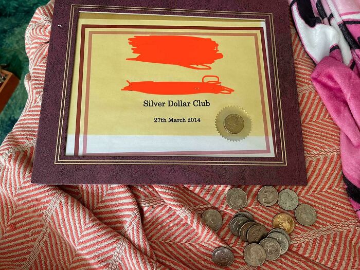 Framed Silver Dollar Club certificate dated 2014 surrounded by loose silver and gold coins on patterned fabric.
