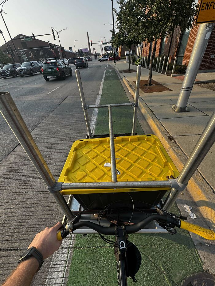 Person cycling on city street bike lane carrying a yellow storage bin as a dumpster diving treasure haul.