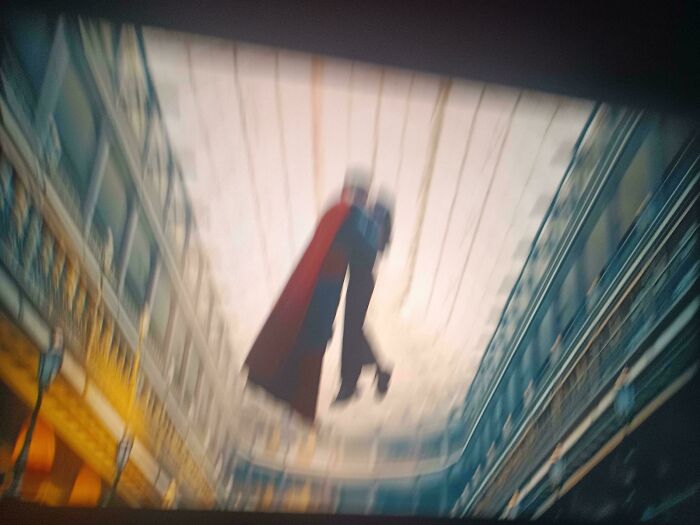 Blurry image of a superhero in a red cape flying inside a large, multi-level shopping mall, showcasing bad movie details.
