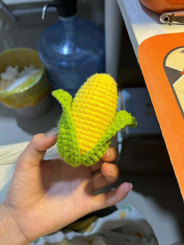 Hand holding a detailed crochet corn with yellow kernels and green husk, showcasing impressive crochet craftsmanship.