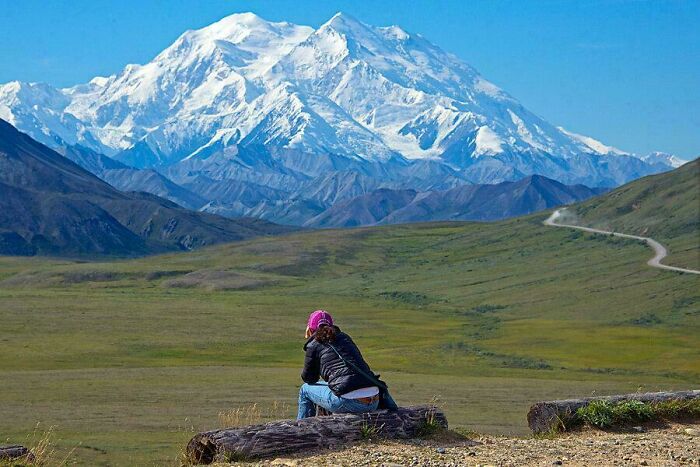 A lone person sits overlooking an extremely large and majestic snow-capped mountain, highlighting the scary and eerie vastness.