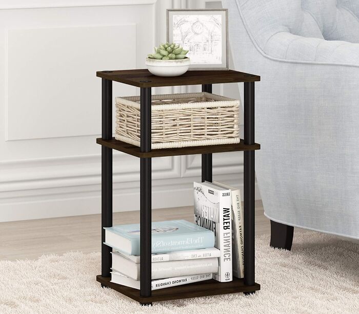 Compact tiny apartment furniture side table with shelves holding books, a wicker basket, and decorative plant near sofa.