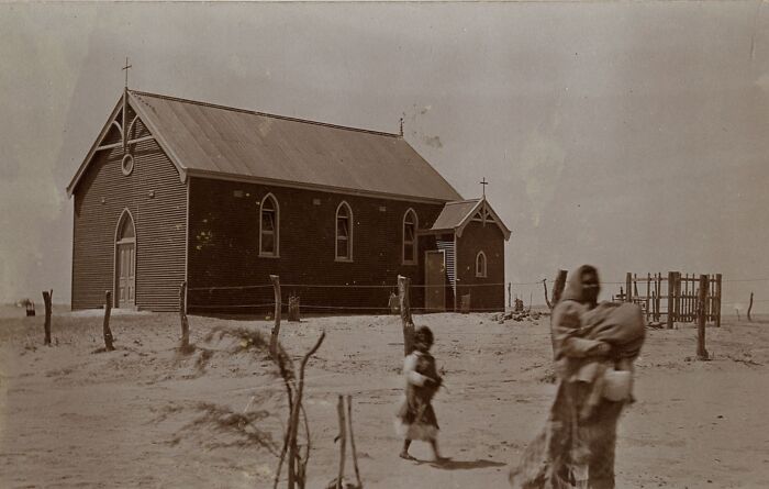 Early 1900s Indigenous Australians near a wooden church in a barren landscape showing rare glimpses through historic photos.