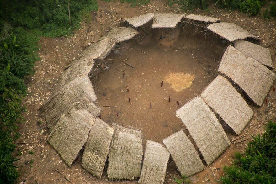 Aerial view of a traditional village with thatched huts arranged in a circle in a forest clearing, interesting community post.