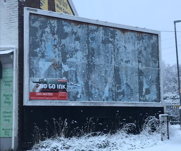 Worn and peeling outdoor advertising billboard on snowy roadside showing a humorous advertising fail.