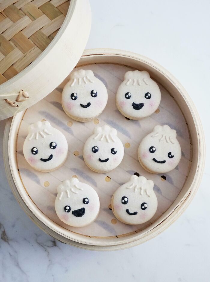 Cute steamed bun-shaped macarons with smiling faces in a bamboo steamer, showcasing incredible bakes with creative designs.