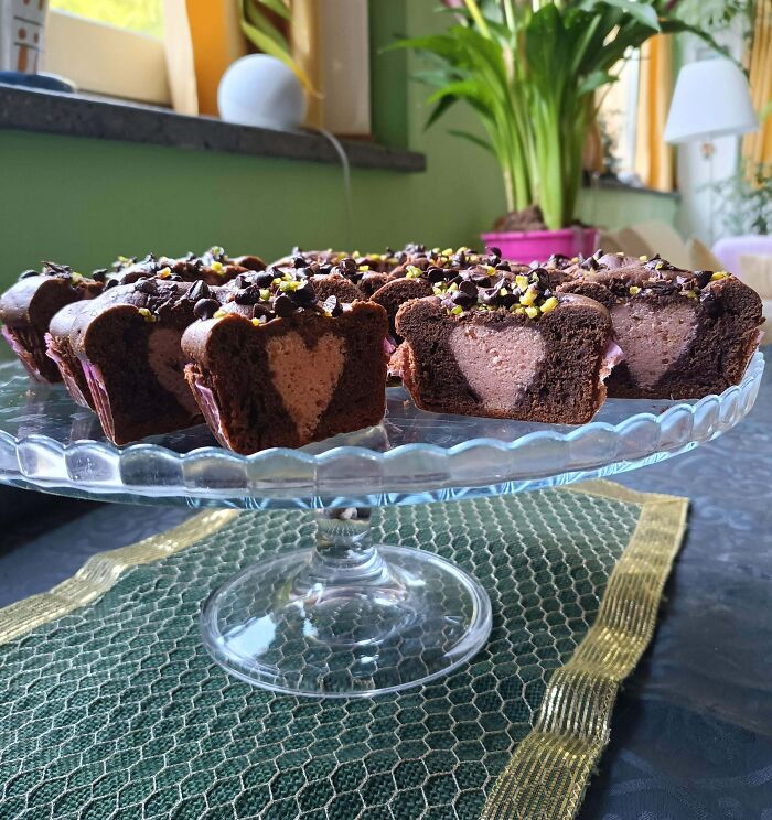 Chocolate bakes with heart-shaped filling and sprinkled toppings arranged on a glass cake stand in a cozy setting.