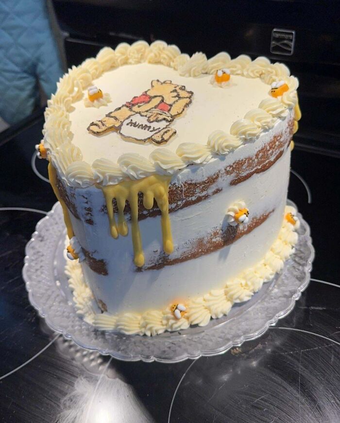 White layered cake with honey drips and bee decorations, featuring a cute bear design, an incredible bake deserving spotlight.