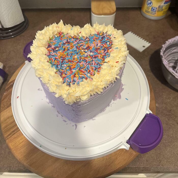 Heart-shaped cake with purple frosting, cream border, and colorful sprinkles, an incredible bake ready to impress.