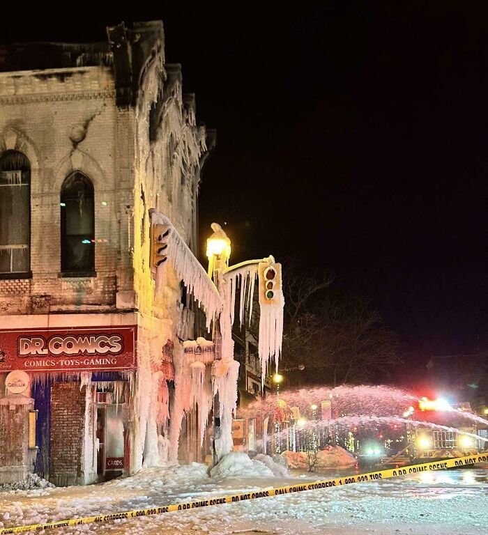 Icicles and frozen water cover a building and street, showcasing wild Mother Nature's power in icy conditions at night.