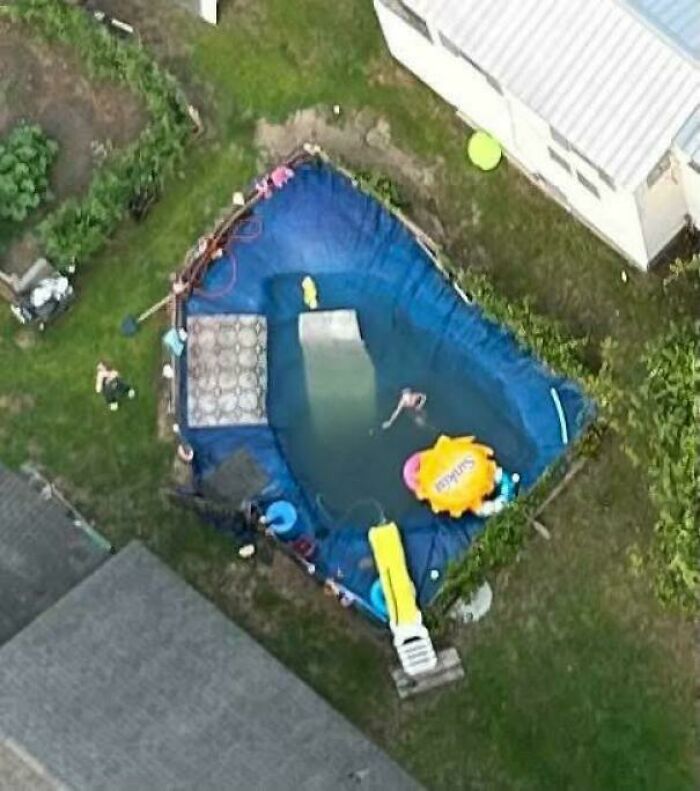 Aerial view of a homemade backyard pool with a slide and inflatable toys, showcasing redneck engineering creativity.
