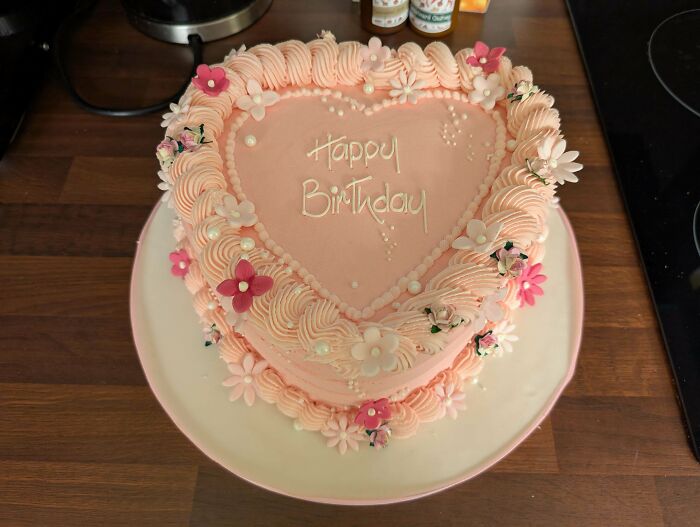 Heart-shaped pink birthday cake decorated with piped frosting and floral accents, showcasing gorgeous baked goods.