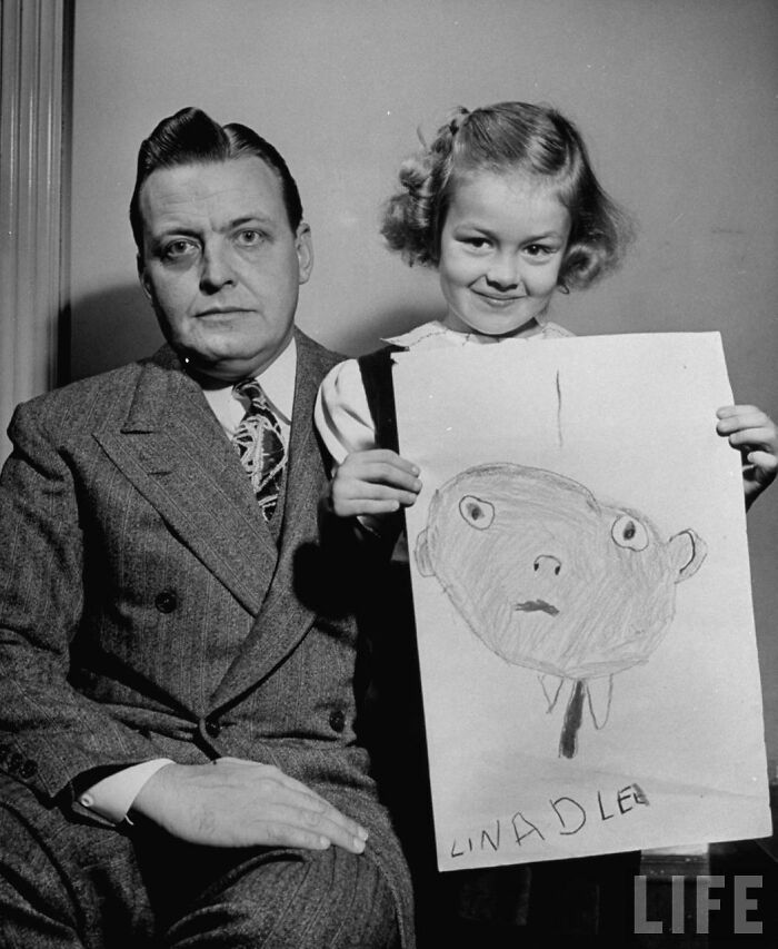 Girl holding a drawing of her dad from memory in 1949, sitting next to the man she sketched in an unintentionally hilarious style.
