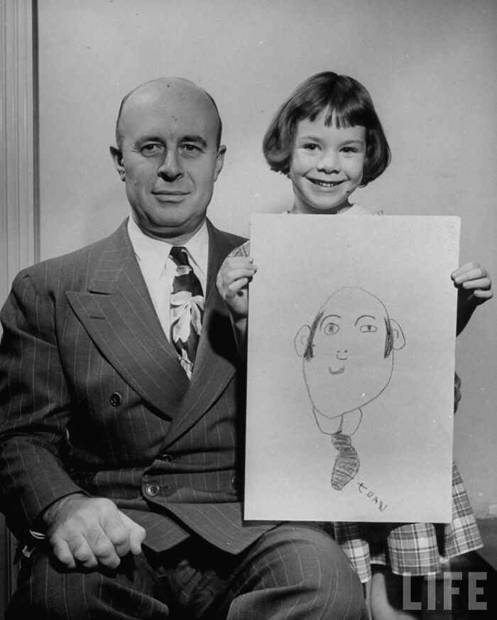A young girl from 1949 proudly shows an unintentionally hilarious drawing of her dad from memory, sitting beside him.