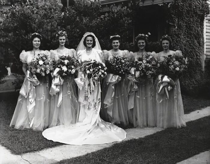 Bride and bridesmaids from the 1940s holding large bouquets in a vintage wedding photo capturing love in the shadow of war.