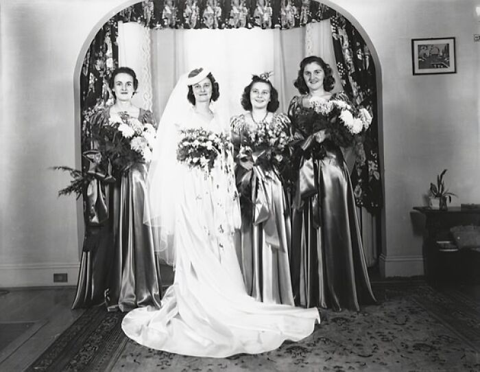 1940s moving wedding photo showing bride and bridesmaids in elegant dresses holding bouquets indoors.