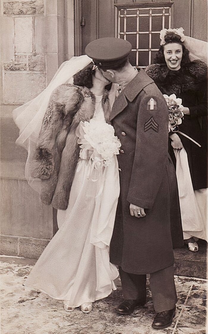 Bride and groom share a kiss in a moving 1940s wedding photo with war-era military uniform and vintage attire.