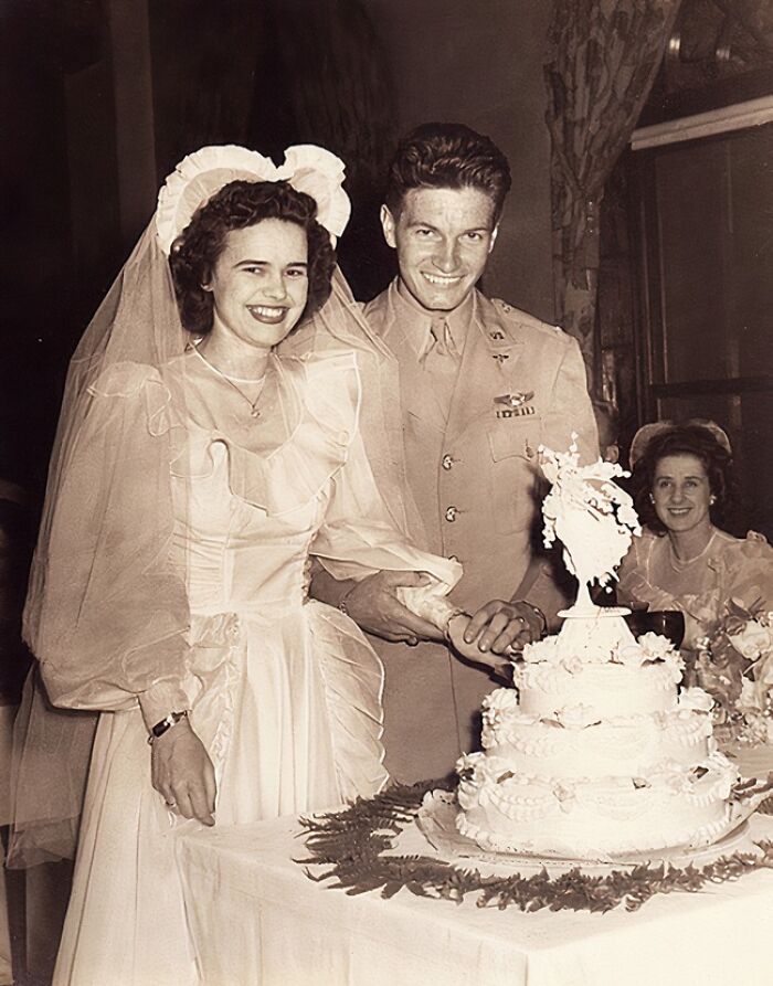 1940s wedding couple cutting cake, bride in vintage gown and groom in military uniform, capturing love in war era.