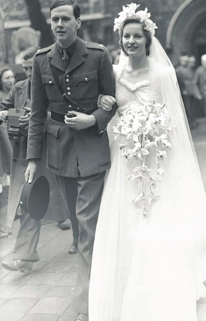 Bride in a vintage wedding dress with a bouquet, walking arm-in-arm with a groom in 1940s military uniform wedding photo.