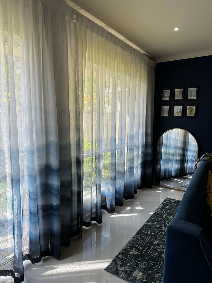 Proudly decorated home corner with blue ombre curtains, cozy sofa, patterned rug, and a decorative mirror on dark wall.