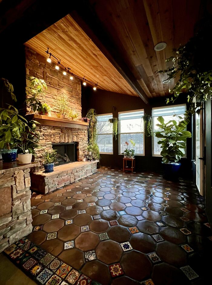 Cozy home corner with stone fireplace, decorative tiled floor, and lush green plants showcasing proud home decorating.